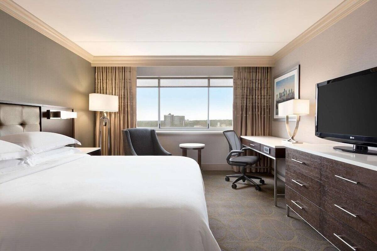 A hotel room with a large bed, a desk with a computer, a TV, and a window with a city view.