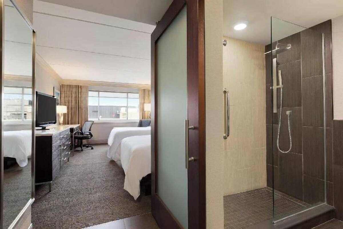 A hotel room with a bed, desk, chair, and a glass-enclosed shower.