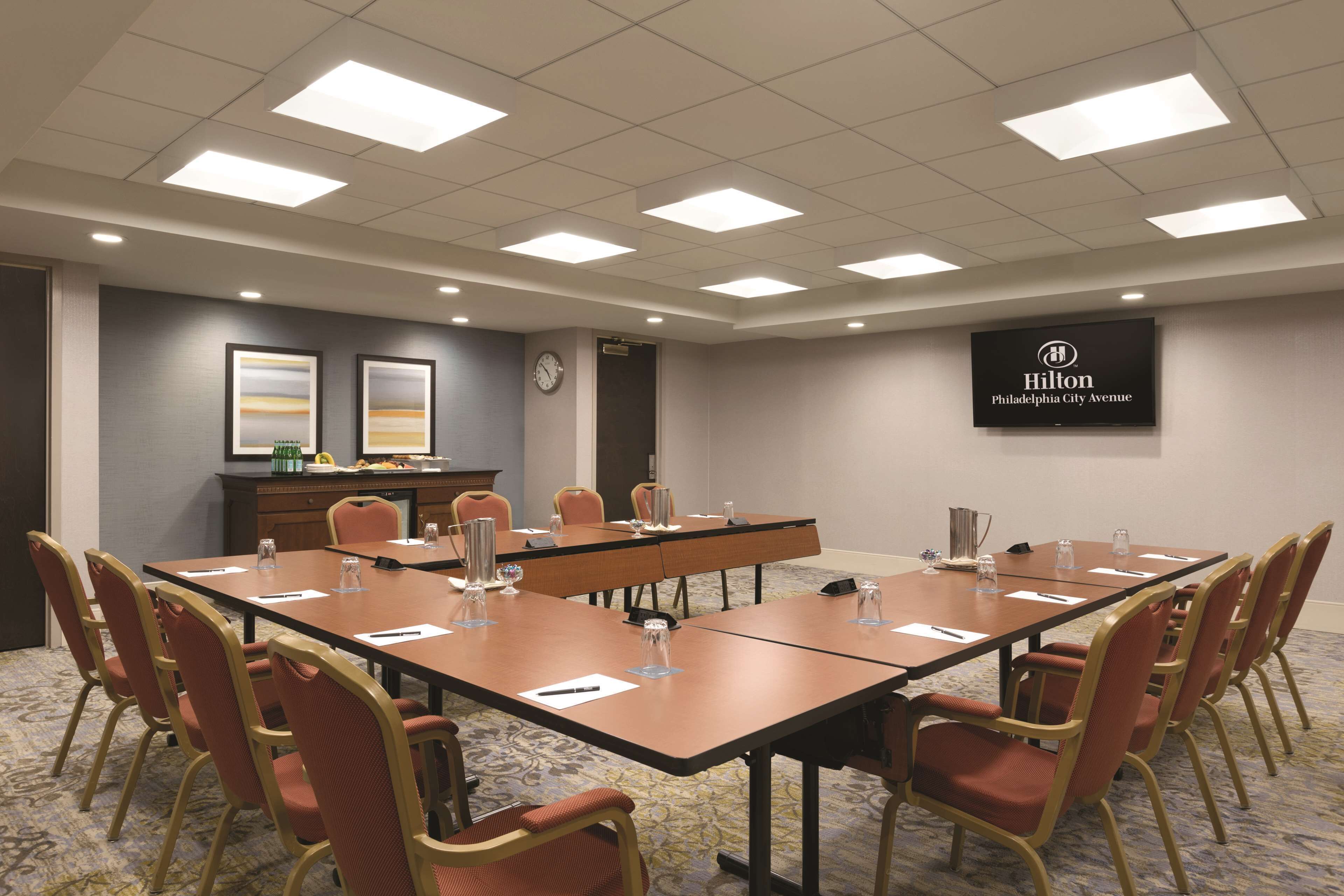 A conference room with a long table, chairs, a clock, and a Hilton sign on the wall.