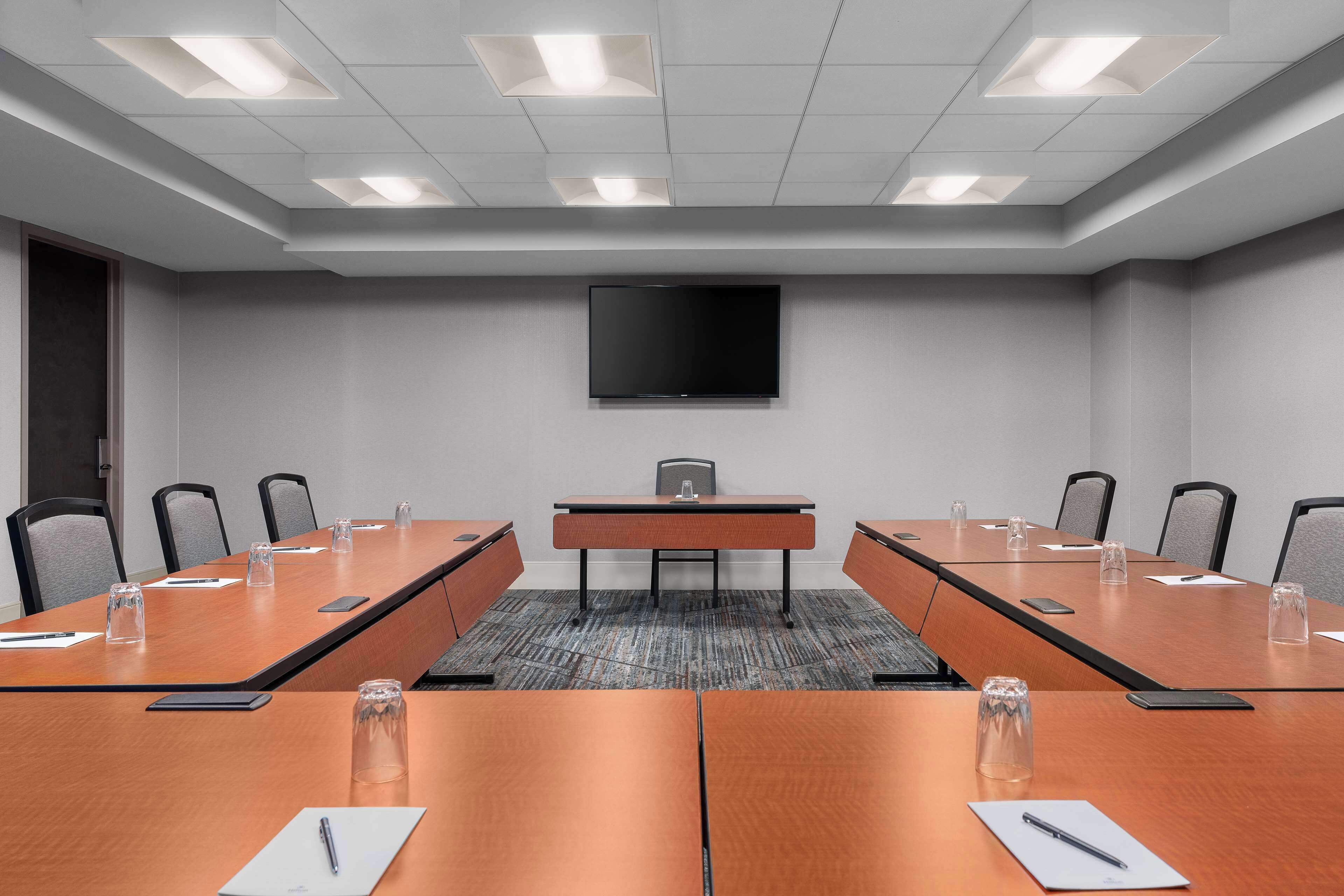Una sala conferenze con un lungo tavolo, sedie, un televisore a schermo piatto e un pavimento rivestito di moquette.