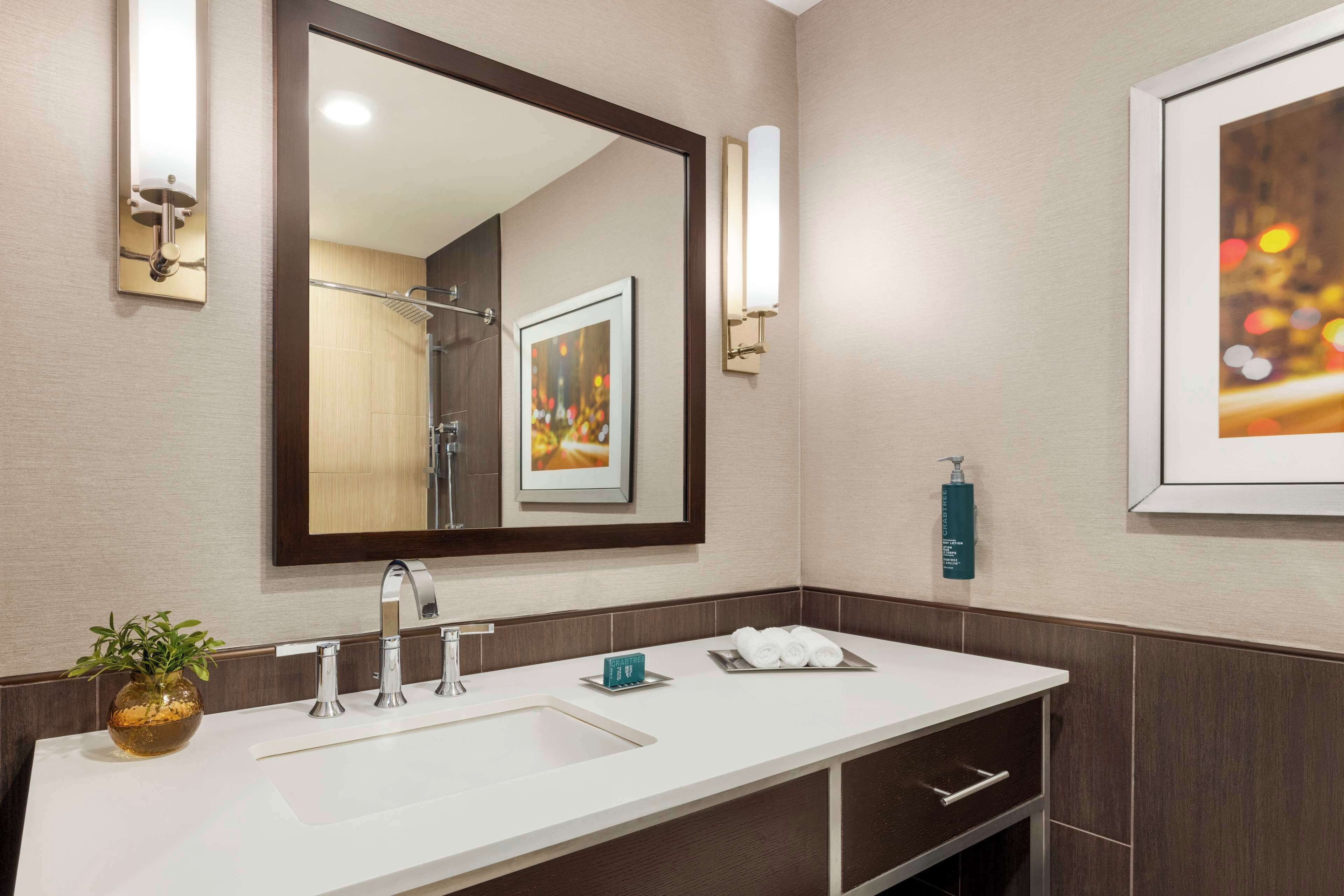 Un baño moderno con un espejo grande, un lavamanos, un perchero para toallas e imagen en un marco en la pared.