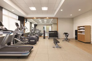 Un gimnasio con cintas de correr, elípticas, una banca y un televisor montado en la pared.