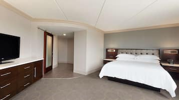Una habitación de hotel moderna con una cama grande, un televisor de pantalla plana, un aparador de madera y un vestidor.