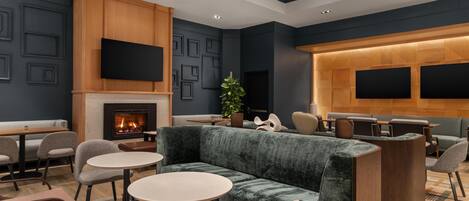 A modern lounge area with a fireplace, seating arrangements, and a large wall-mounted TV screen.