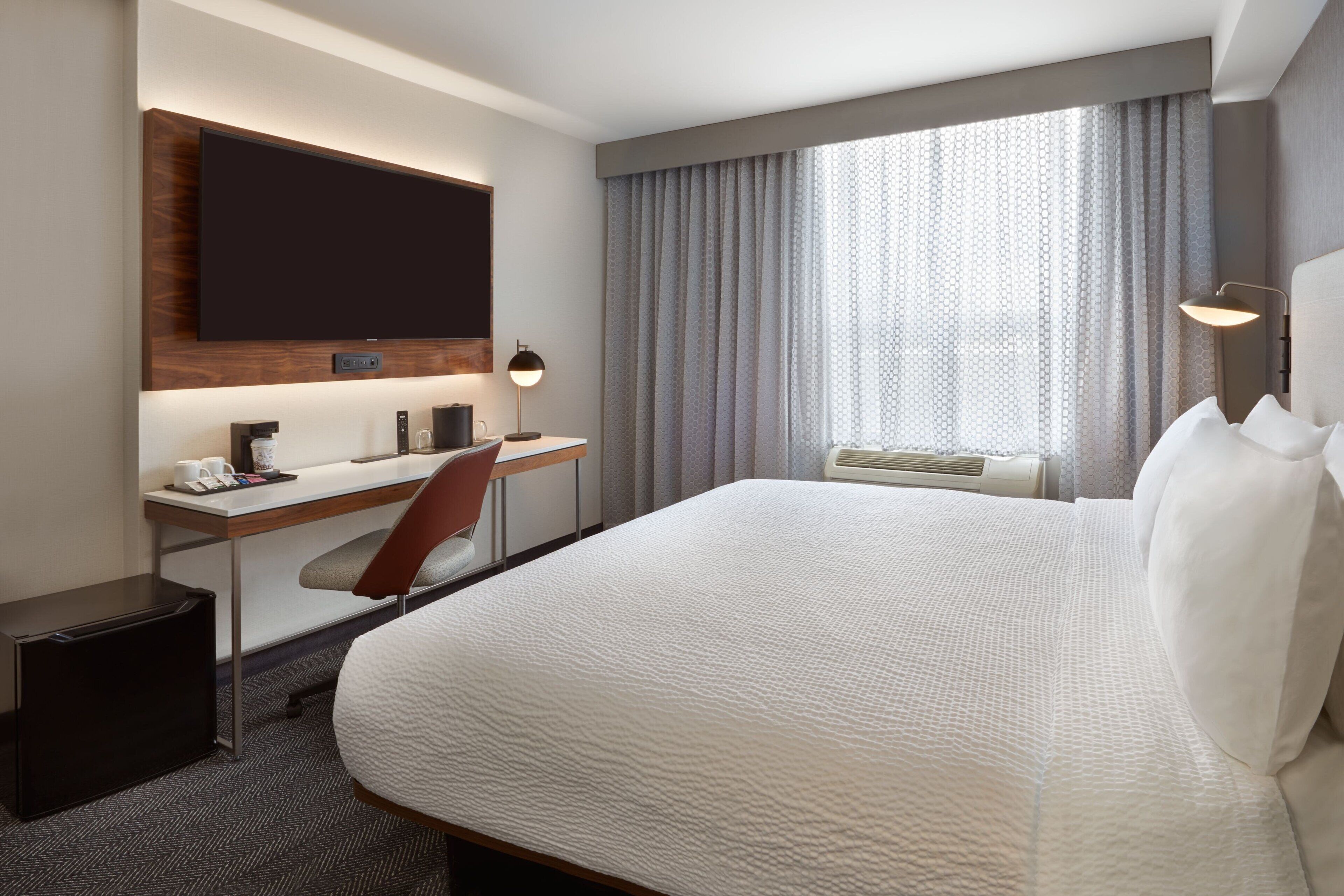 Habitación de hotel con una cama grande, un escritorio con silla, televisor de pantalla plana en la pared y una ventana con cortinas.