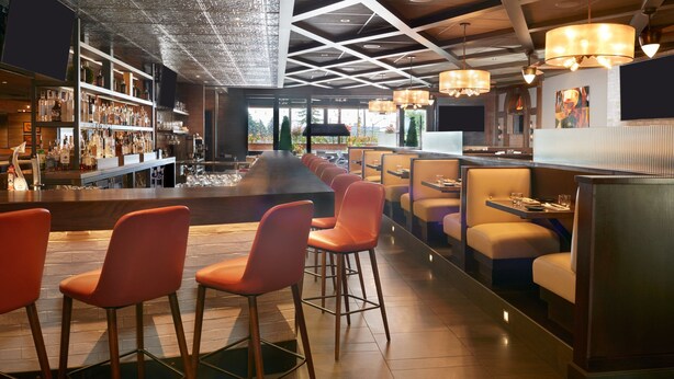 Un bar moderno con una barra larga, diferentes opciones de asientos y un techo decorativo.
