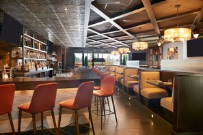 A modern bar area with a long counter, multiple seating options, and a decorative ceiling. - Courtyard by Marriott Kitchener (Kitchener)