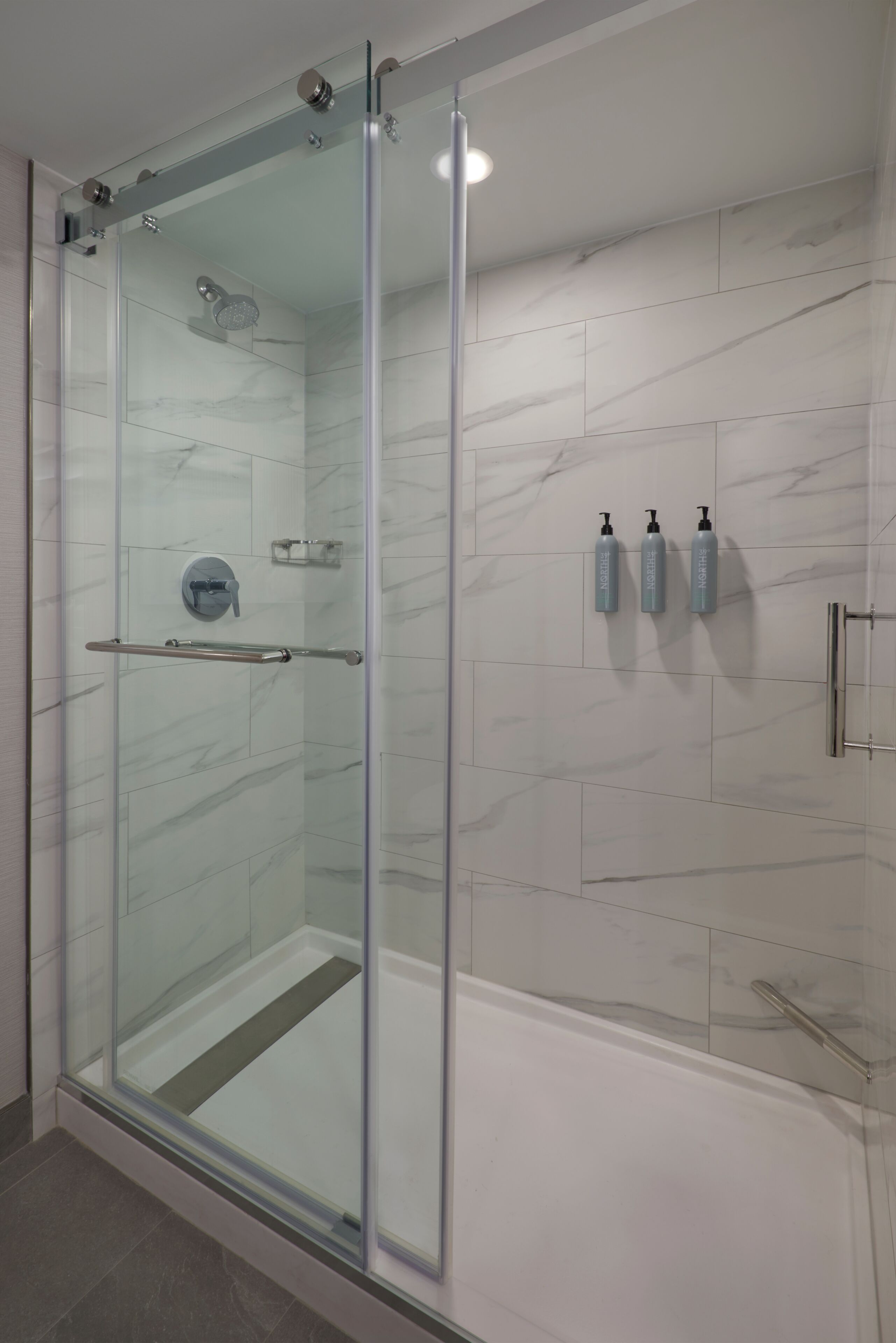A glass-enclosed shower with a handheld showerhead, a glass door, and a towel rack.