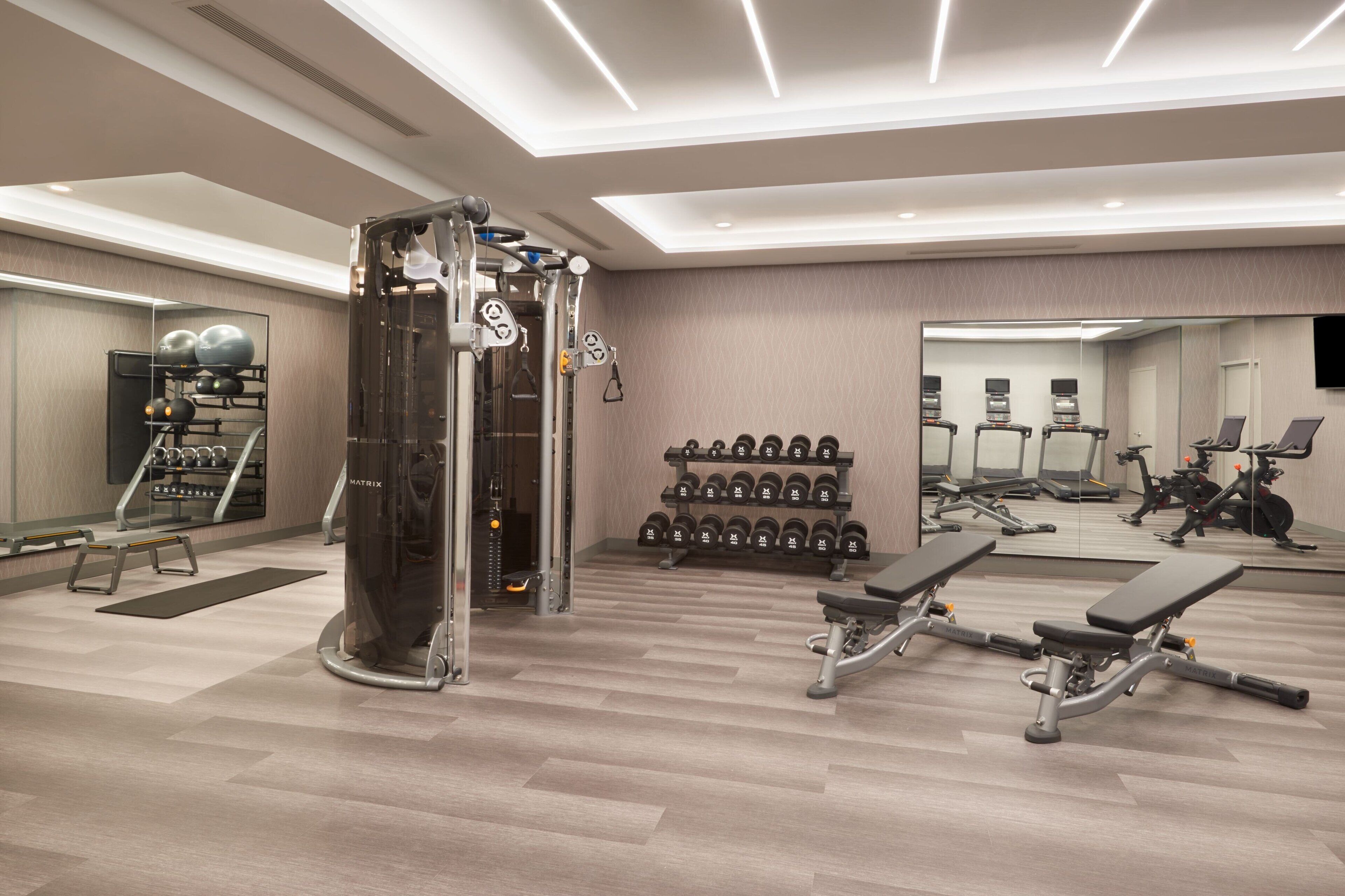A modern gym with a mirrored wall, weight racks, dumbbells, and exercise equipment.