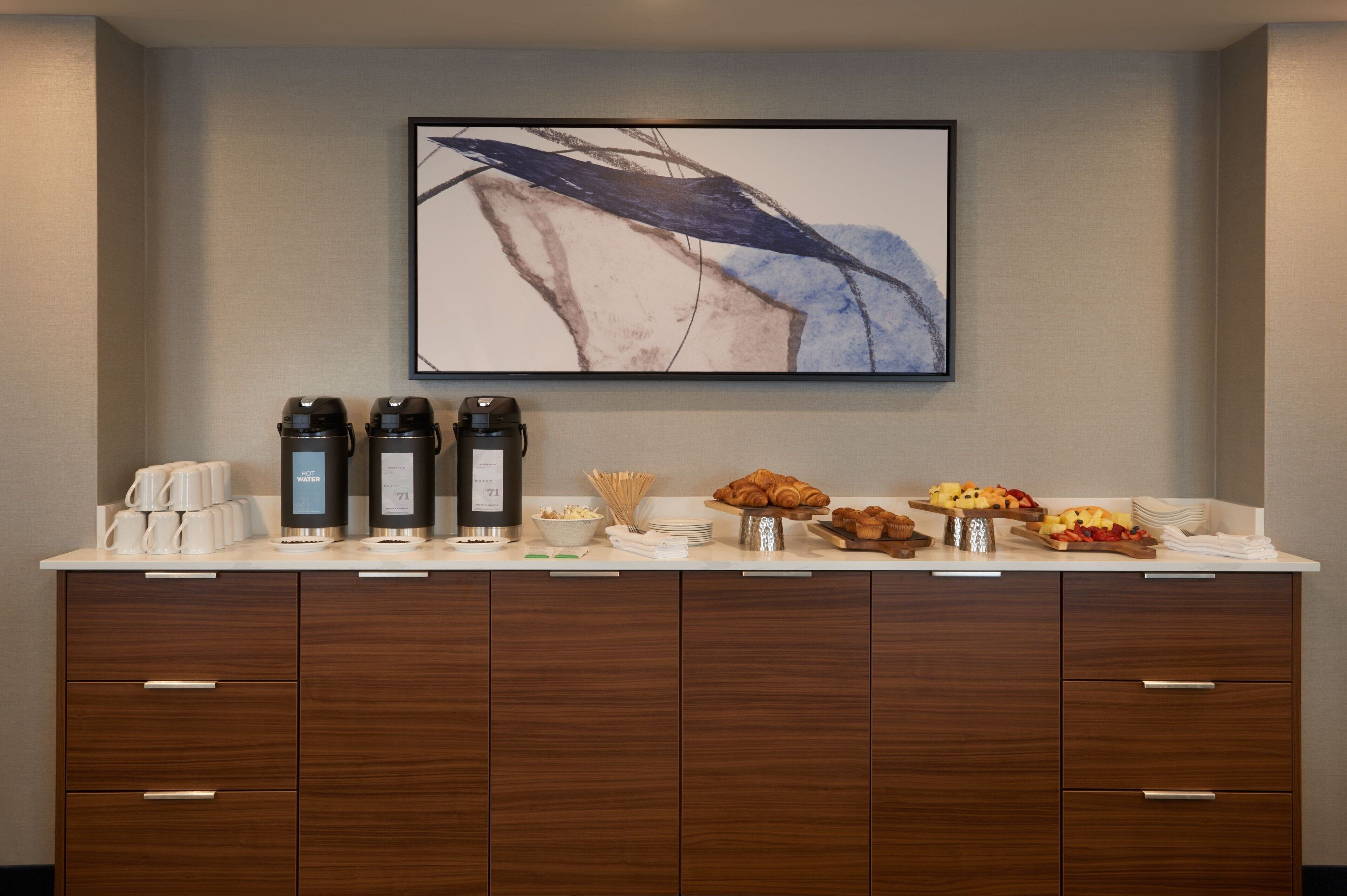 Bar de pequeno-almoço com máquinas de café, croissants e fruta.