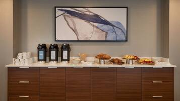 Bar de pequeno-almoço com máquinas de café, croissants e fruta.