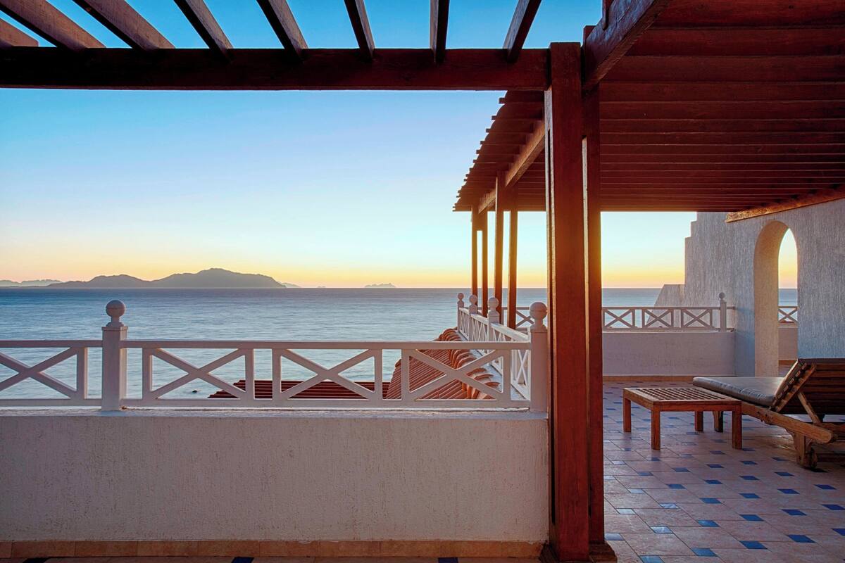 A balcony with a view of the sea and mountains at sunset.