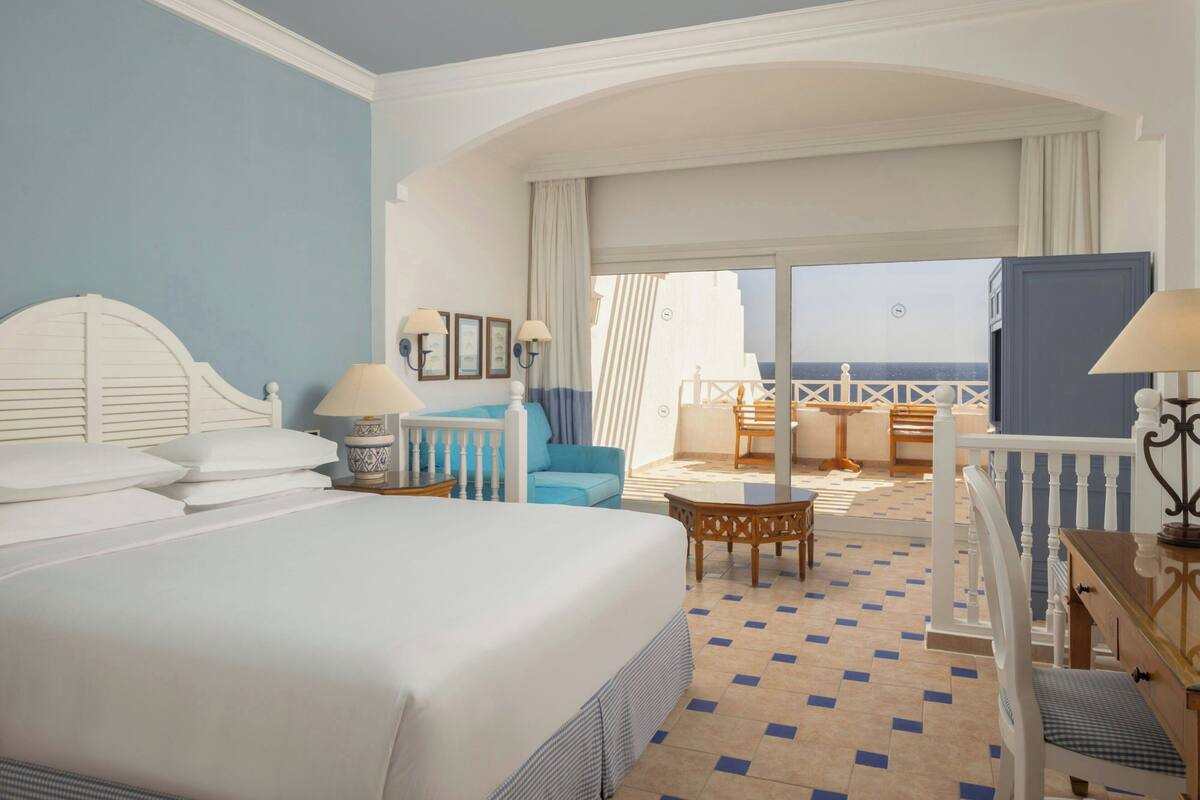 A hotel room with a large bed, a balcony with a view, a desk, and a chair.
