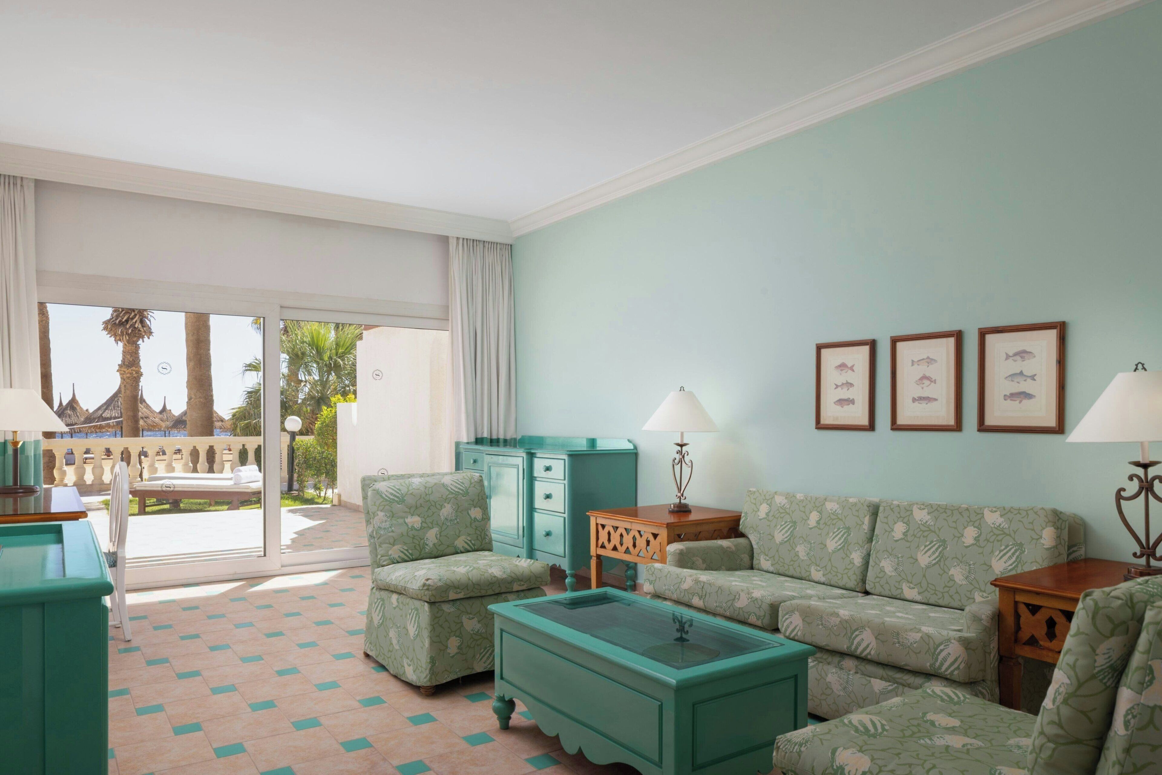 A room with a sofa set, a coffee table, a lamp, and a view of an outdoor area with a balcony.