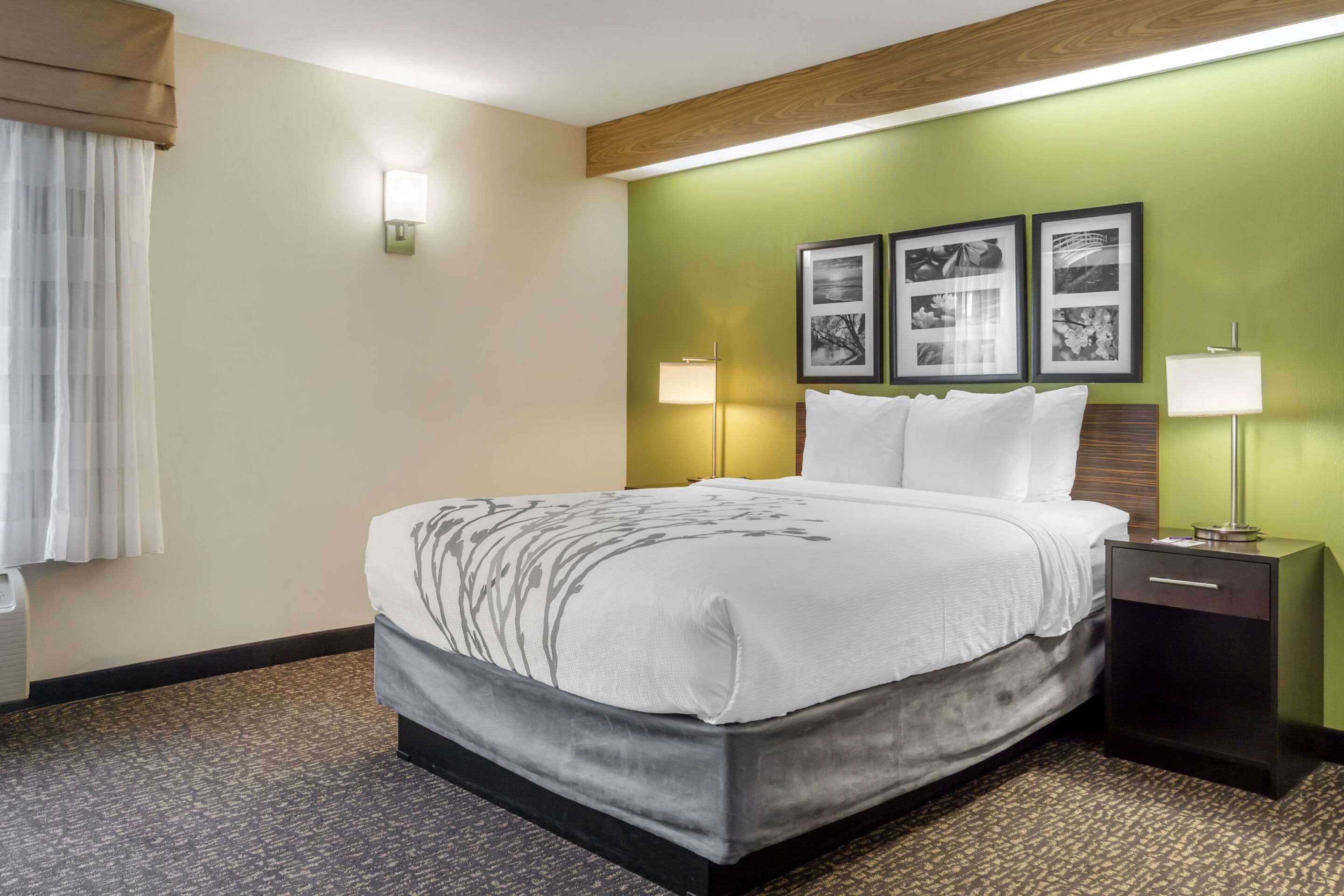 A hotel room with a large bed, two bedside lamps, a nightstand, and three framed pictures on the wall.