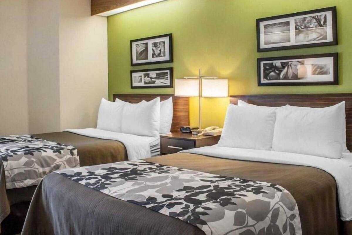 A hotel room with two beds, a nightstand with a lamp, and framed pictures on the wall.