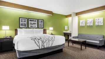A hotel room with a large bed, a grey sofa, a small table, and artwork on the walls.