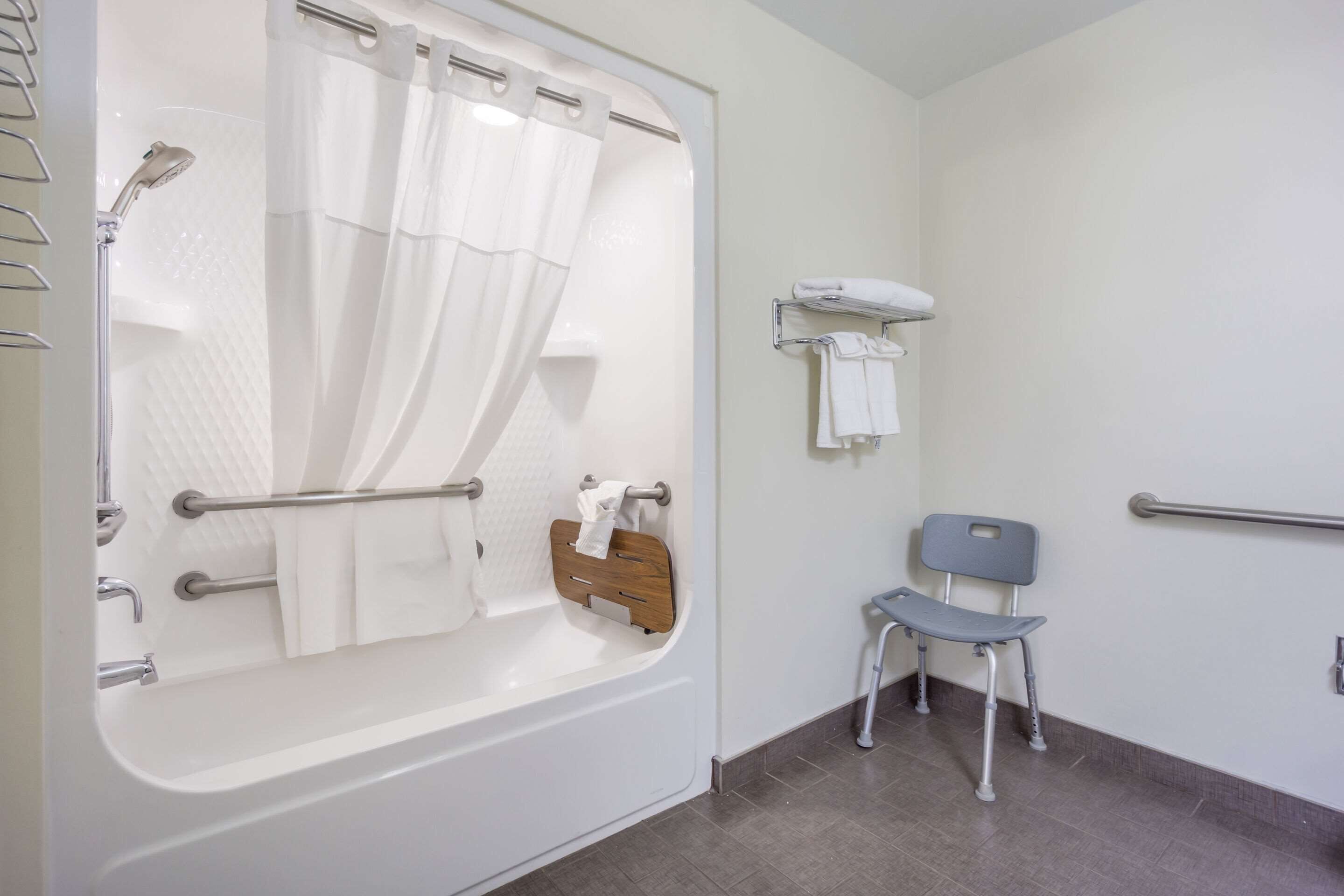 Un baño con bañera, ducha, barra de apoyo, silla y toallero.