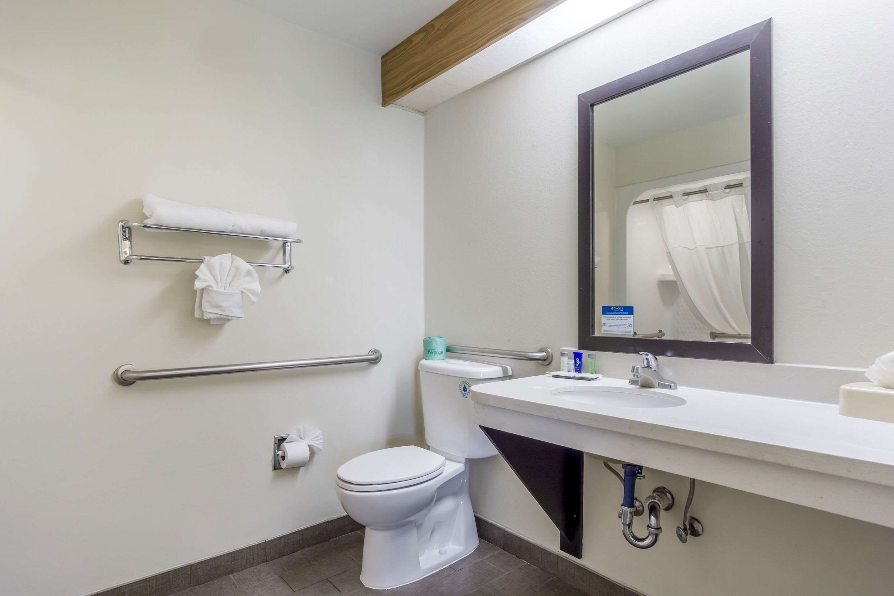 Een badkamer met een wit toilet, een wastafel met een spiegel erboven en een handdoekrek met handdoeken.