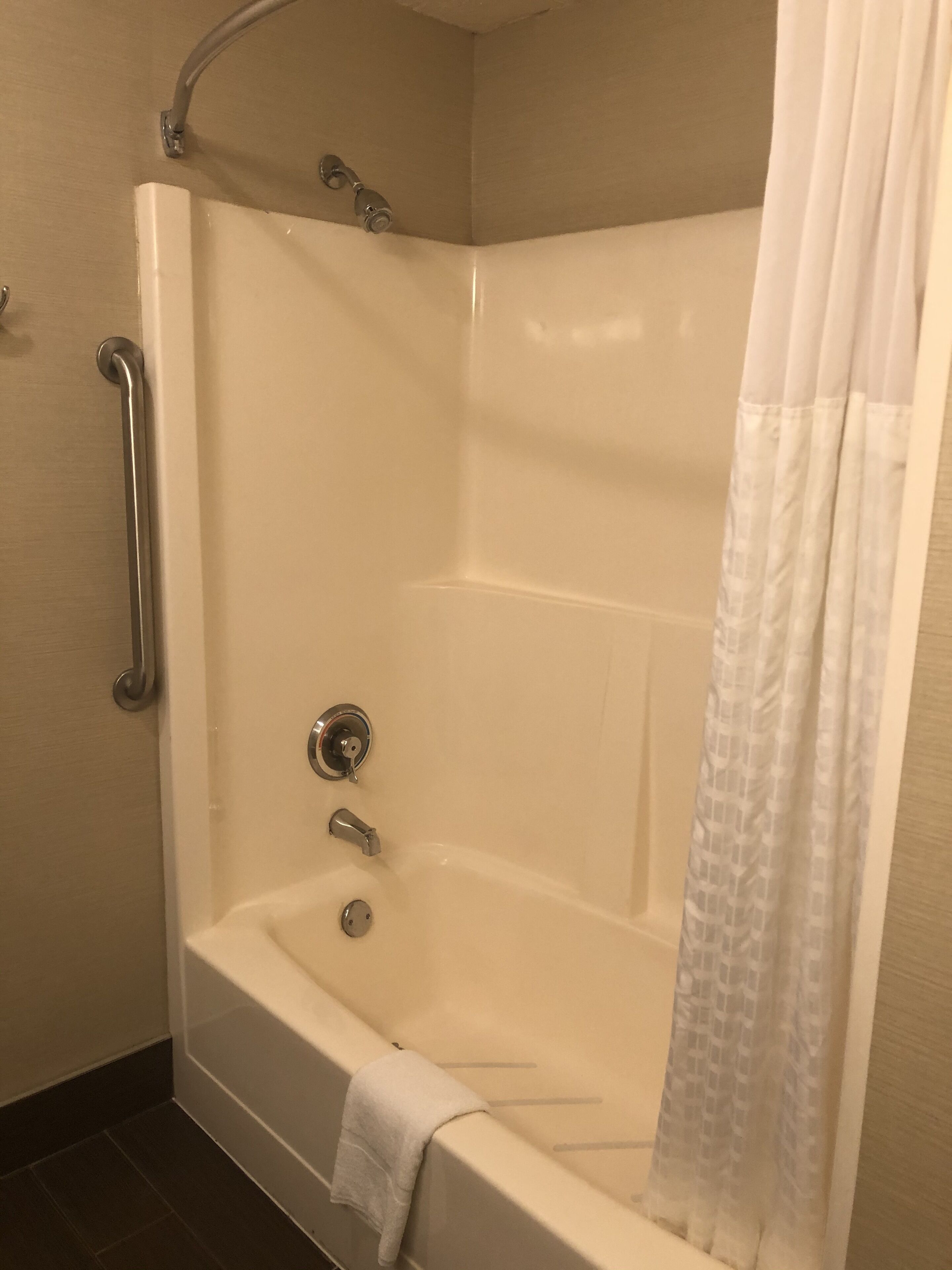 A corner shower with a white bathtub, a handheld showerhead, a handheld faucet, and a towel on the edge.