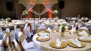 A banquet hall with round tables set for a formal event, featuring white tablecloths, gold napkins, and floral centerpieces. - Sleep Inn - SeaTac Airport (SeaTac)