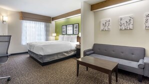 A hotel room with a bed, a sofa, a desk, and artwork on the wall. - Sleep Inn - SeaTac Airport (SeaTac)