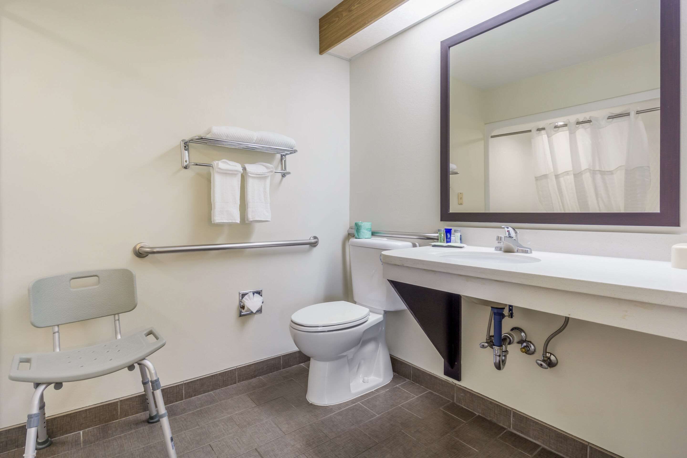 A bathroom with a toilet, a handrail, a towel rack, a mirror, and a shower curtain.