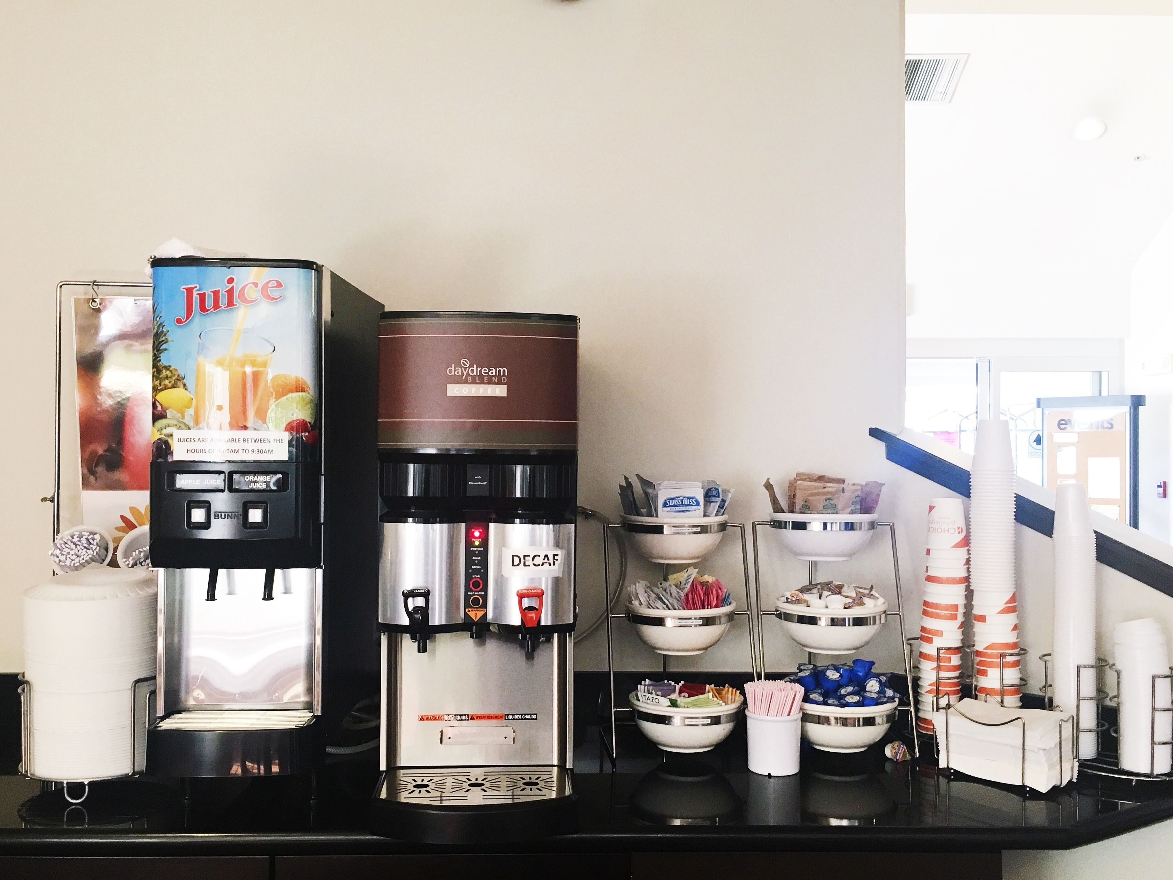 Un espace dédié au café, équipé d'un distributeur de jus, d'une machine à café, ainsi que de divers condiments et ustensiles.