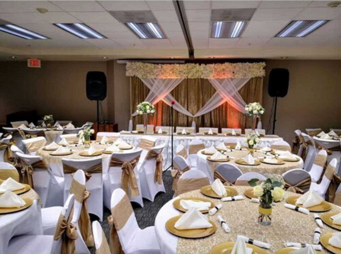 A banquet hall with round tables, white chairs, and gold accents.