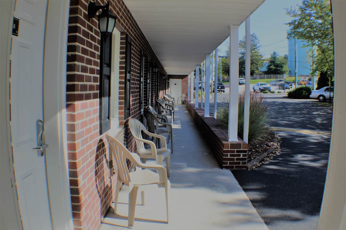A motel with a covered walkway, outdoor seating, and a parking lot.