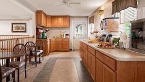 A kitchen with wooden cabinets, a dining table with chairs, and a refrigerator. - Inn at Cemetery Hill (Gettysburg)