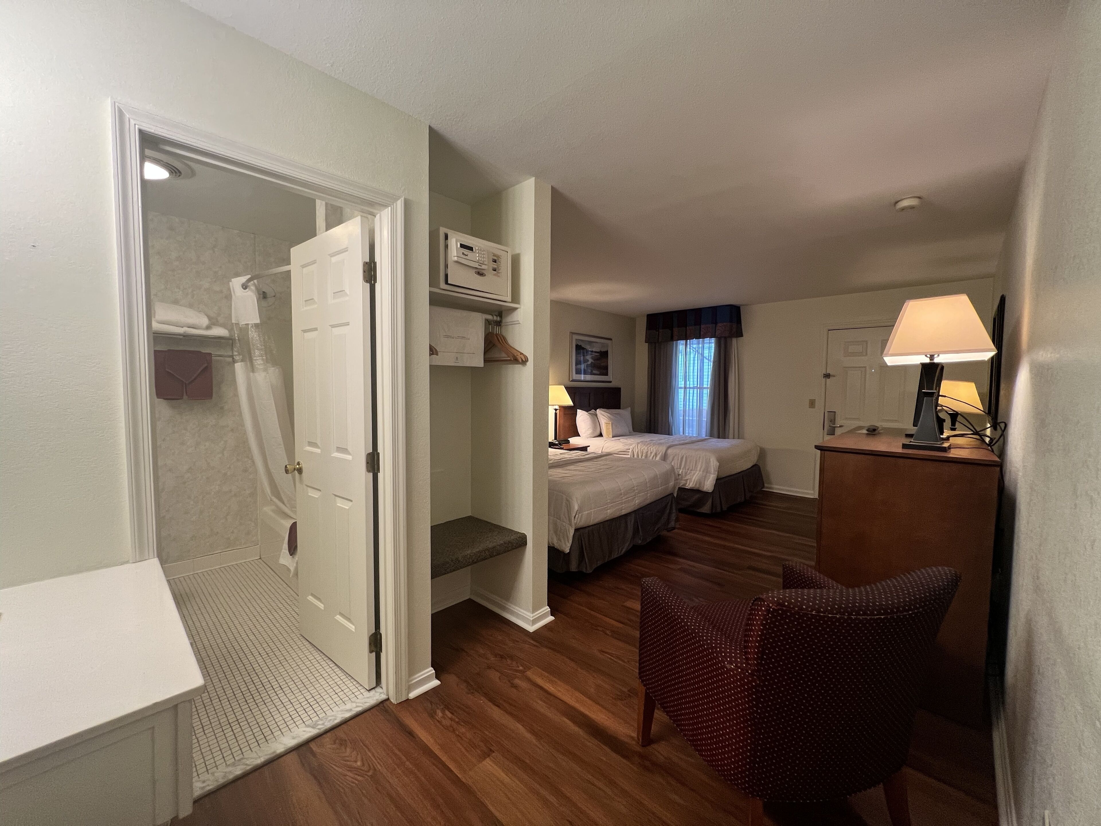 A hotel room with a shower, two beds, a desk, and a chair.