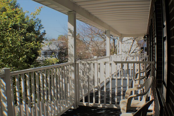 A covered porch with a white railing, a staircase, and several chairs.