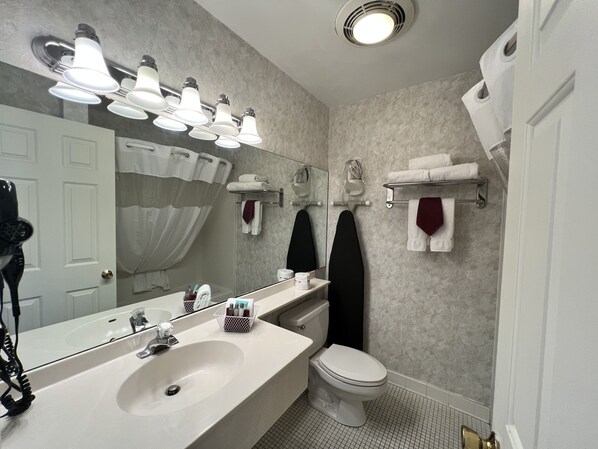 A modern bathroom with a large mirror, white sink, and a toilet. There are multiple towel racks and a shower curtain visible.