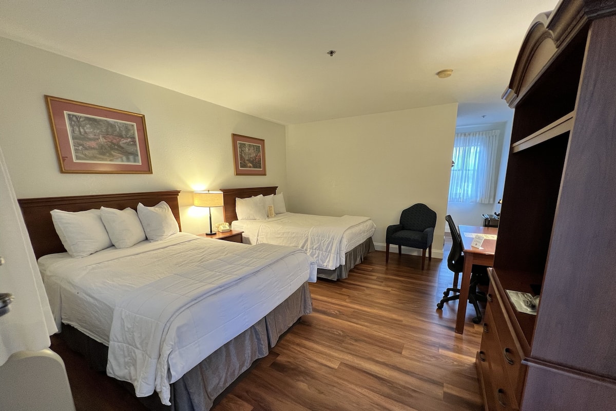 A hotel room with two beds, a desk, a chair, and a wardrobe.