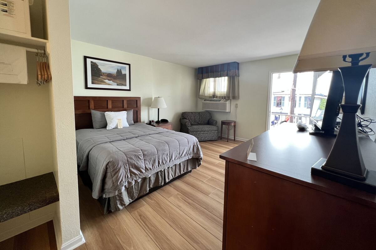 A hotel room with a bed, a desk, a chair, a lamp, and a window.