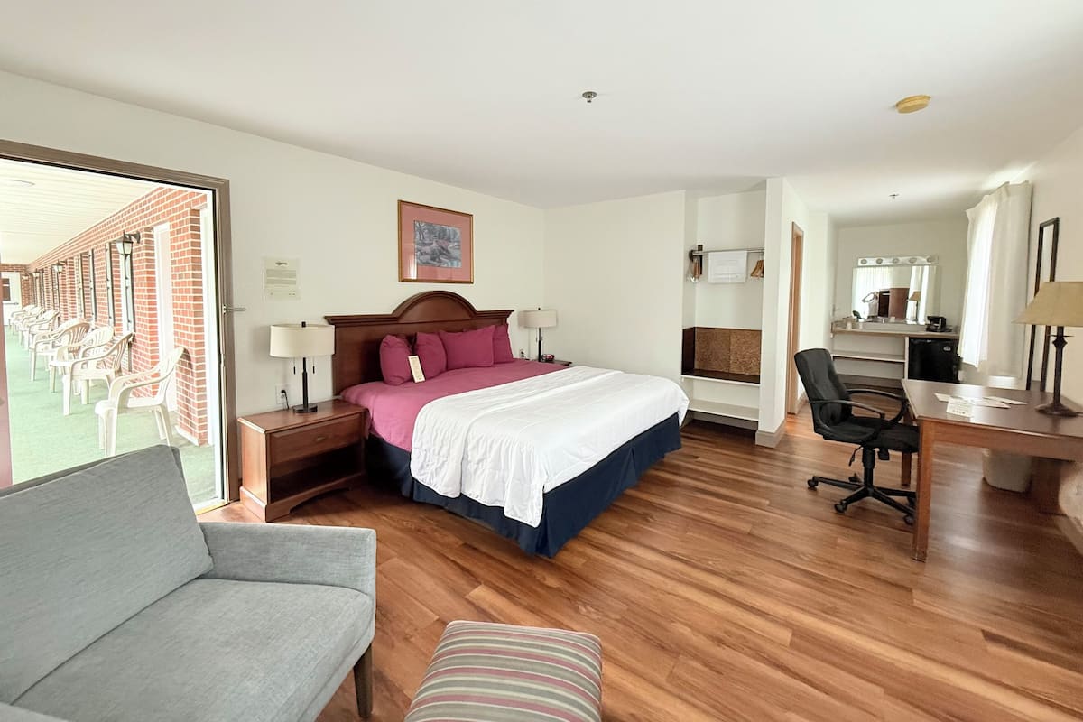 A hotel room with a bed, a desk, a chair, a sofa, and a large window.