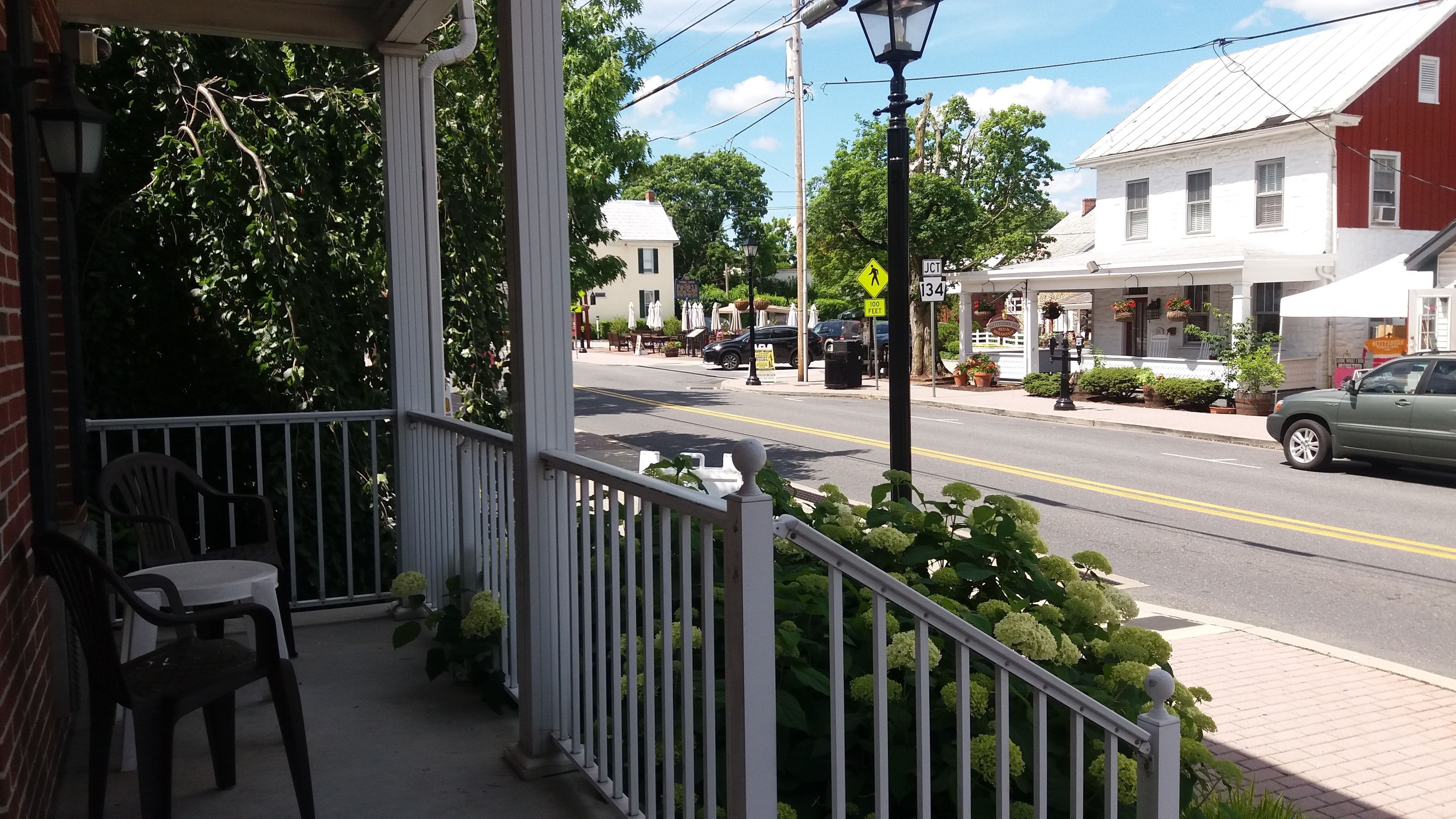 A porch with a railing, outdoor seating, and a street view with buildings and a car.