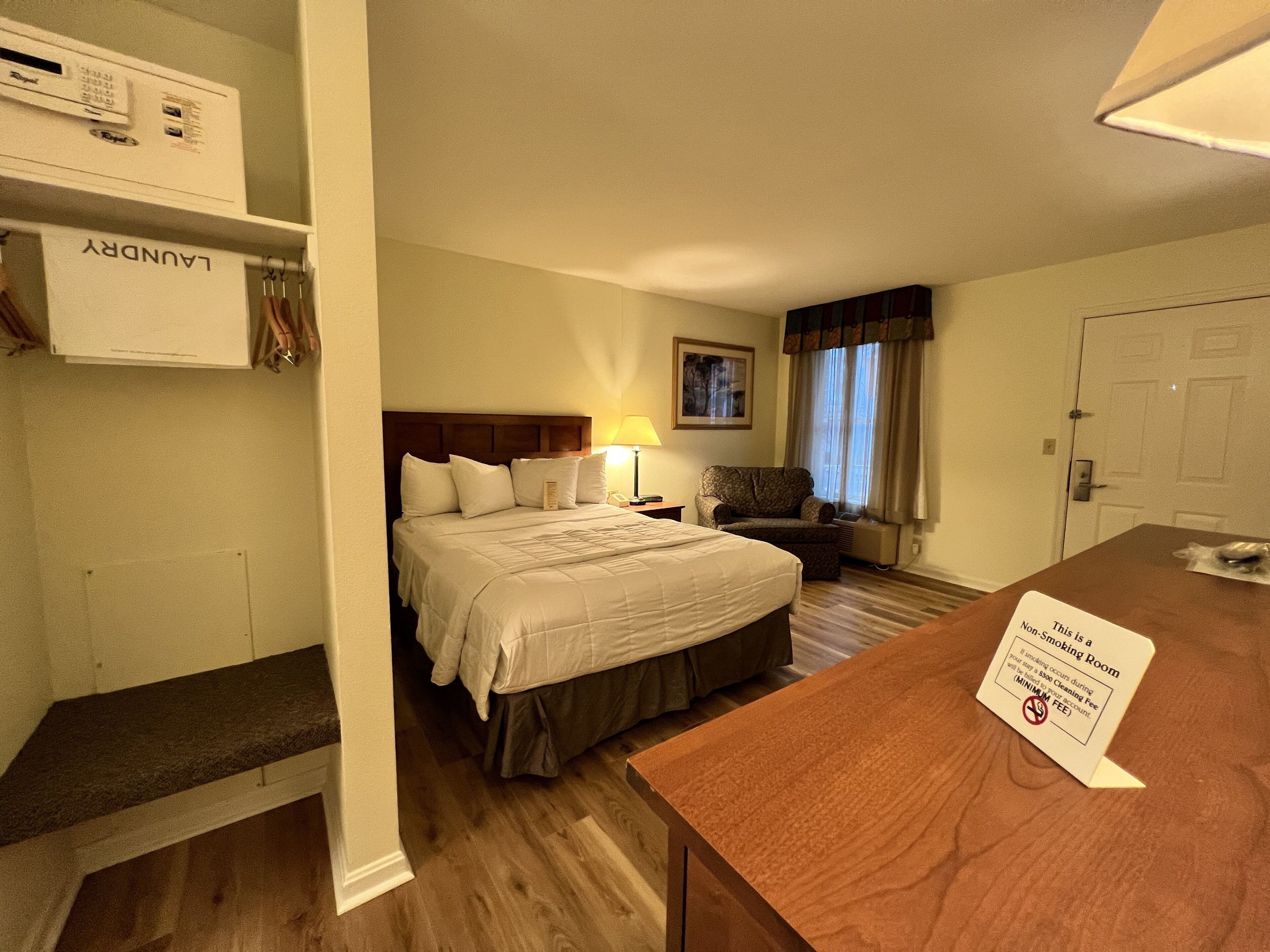 A hotel room with a bed, a desk, a chair, a lamp, and a sign indicating it is a non-smoking room.