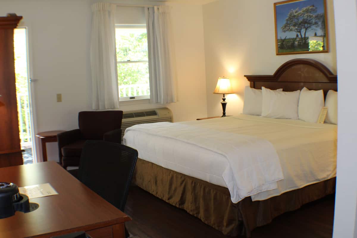 A hotel room with a bed, a desk, a chair, a lamp, and a window with curtains.