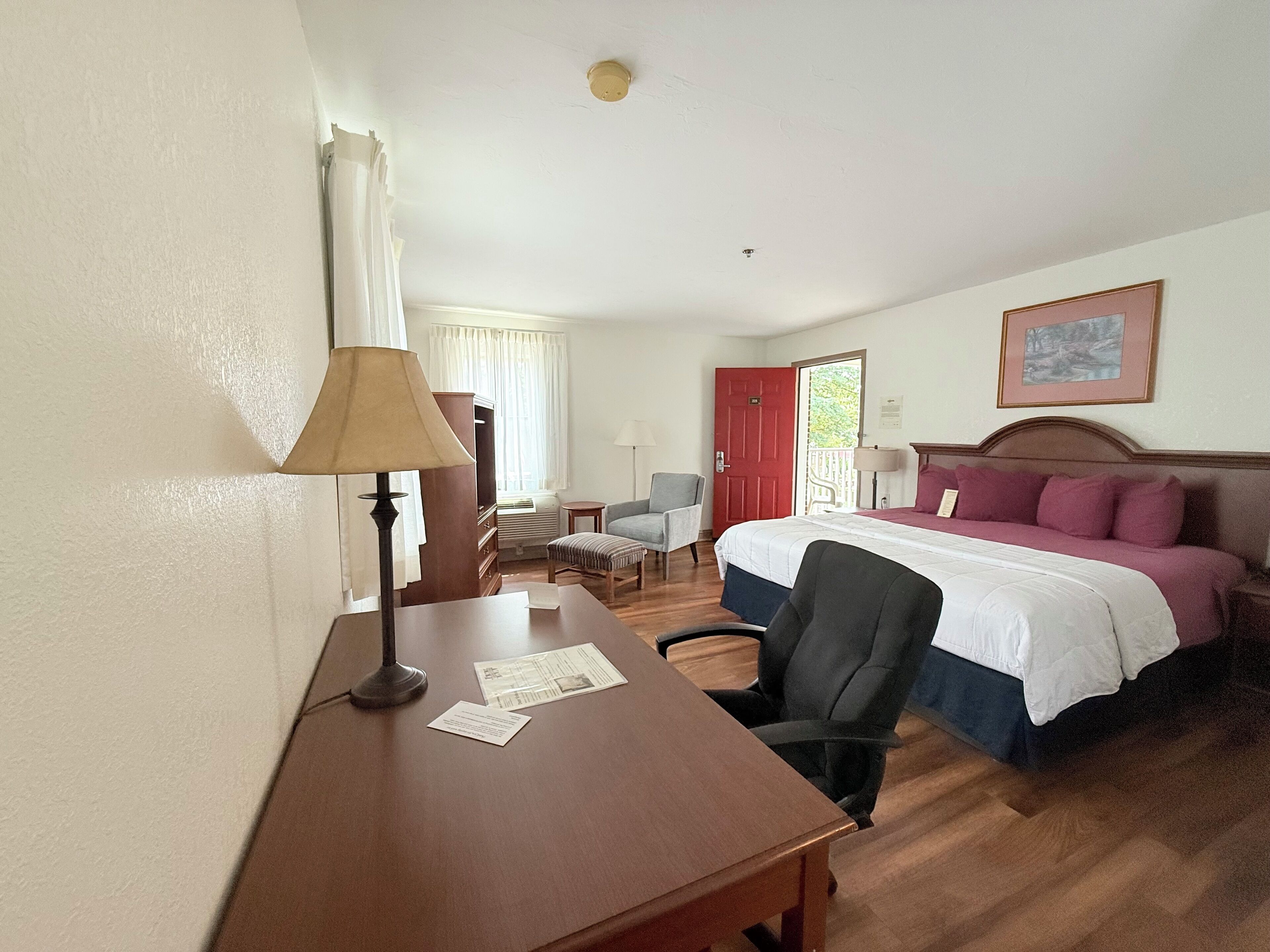 A hotel room with a bed, a desk, a chair, a small table, and a window with curtains.