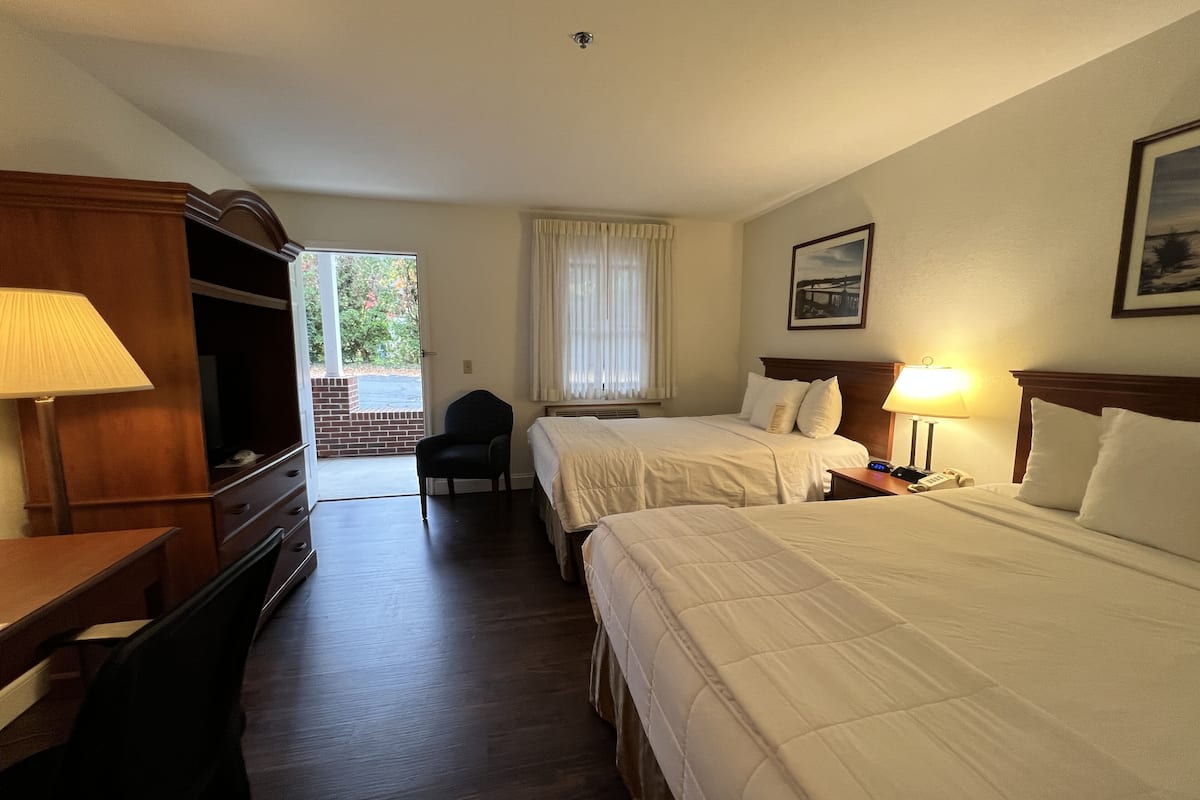 A hotel room with two beds, a desk, a chair, a lamp, and a window with curtains.