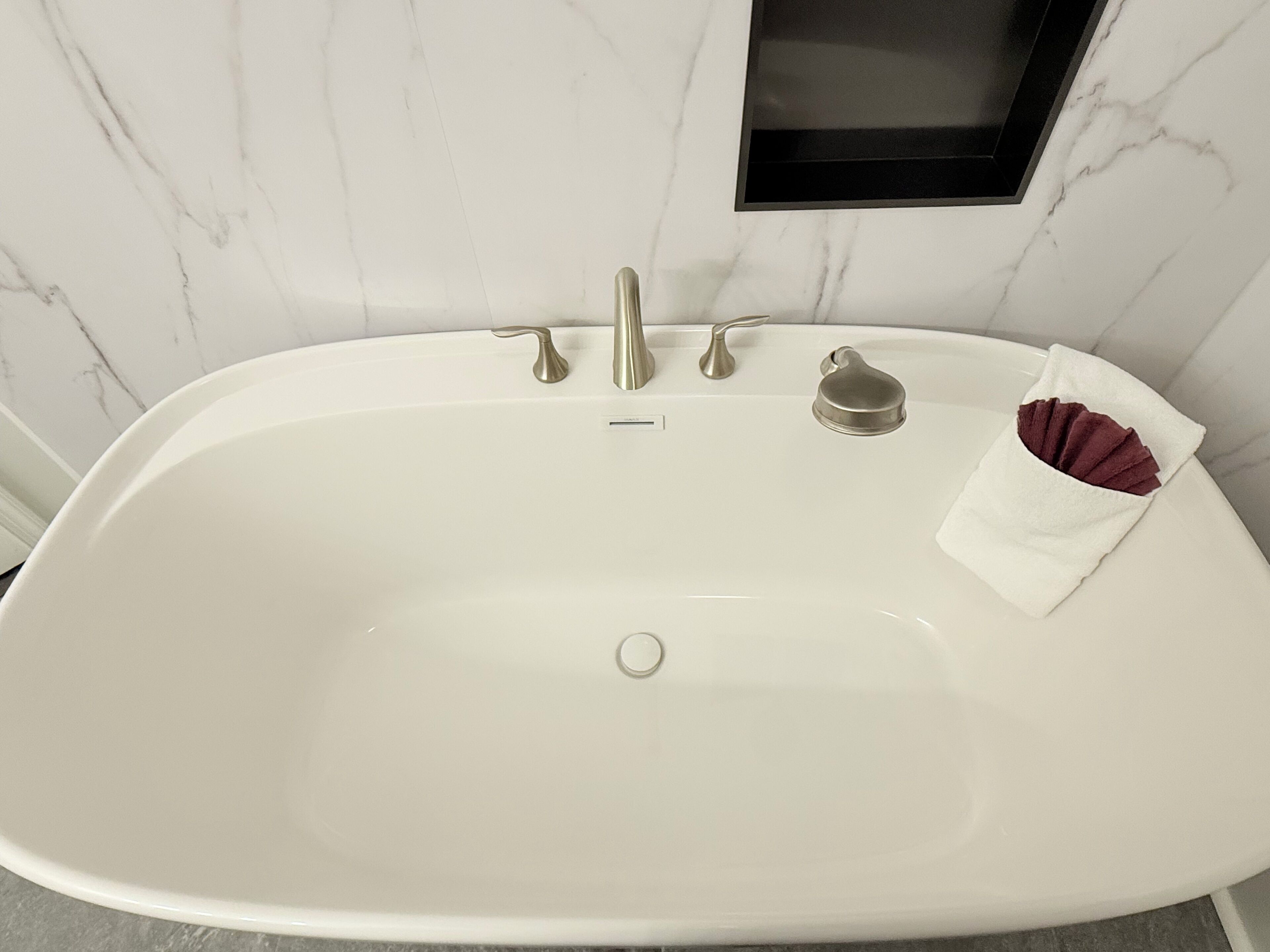 Una bañera blanca independiente con un solo grifo y un desagüe pequeño y redondo.