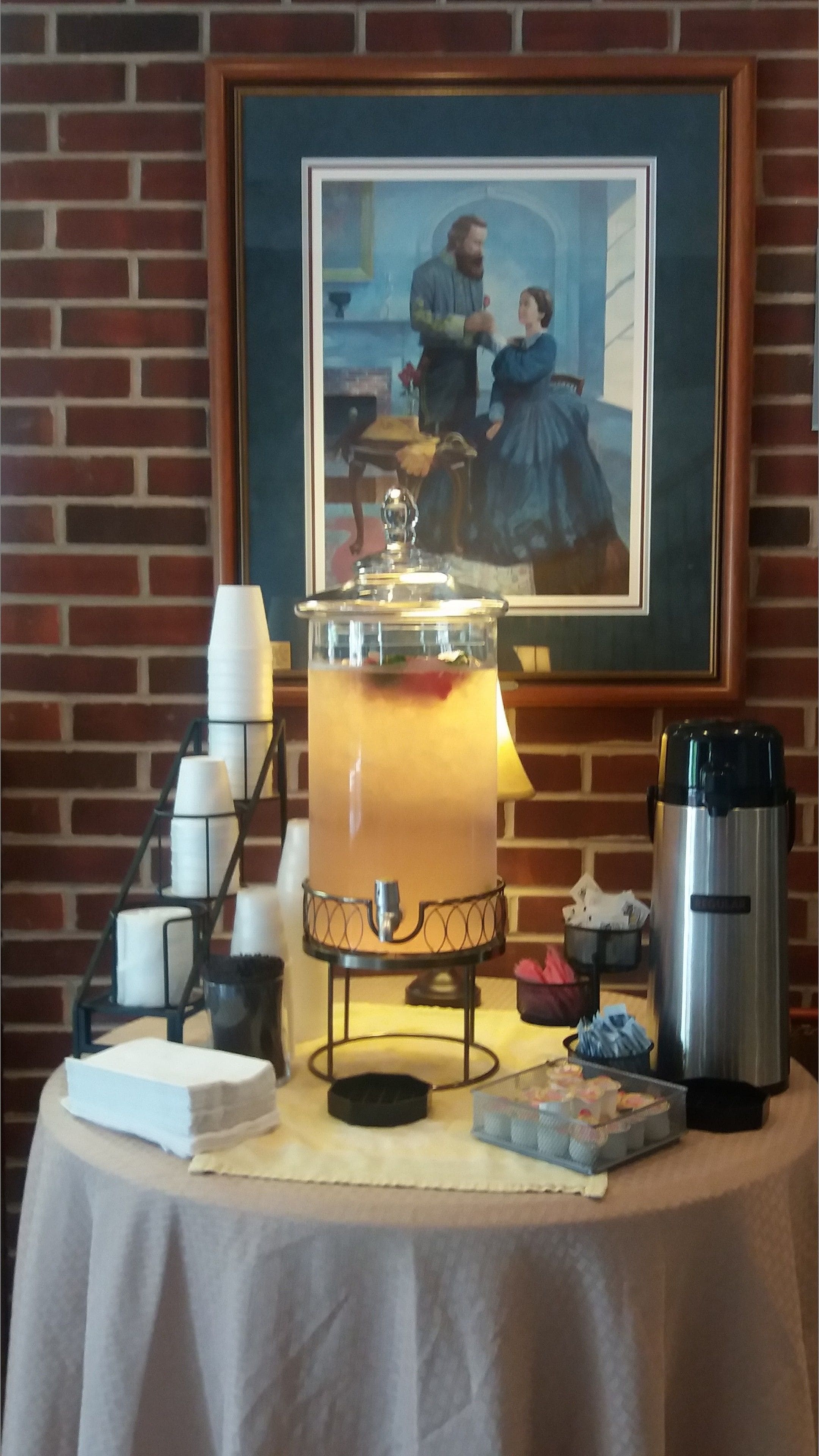 Een tafel met een drankdispenser, een koffiezetapparaat en een lijst met een schilderij.