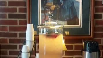 Una mesa con dispensador de bebidas, cafetera y un cuadro enmarcado.