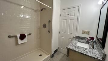 A bathroom with a walk-in shower, a vanity with a sink, and a door leading to another room.