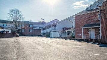 A parking lot with a row of residential buildings, including a two-story house with a balcony and a single-story house with a porch.