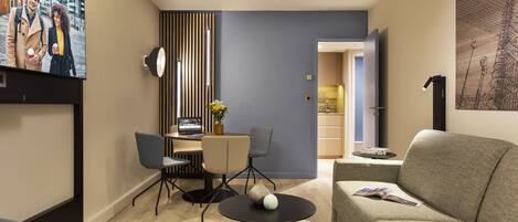Una sala de estar moderna con un sofá, una mesa de comedor con sillas y un televisor montado en la pared.