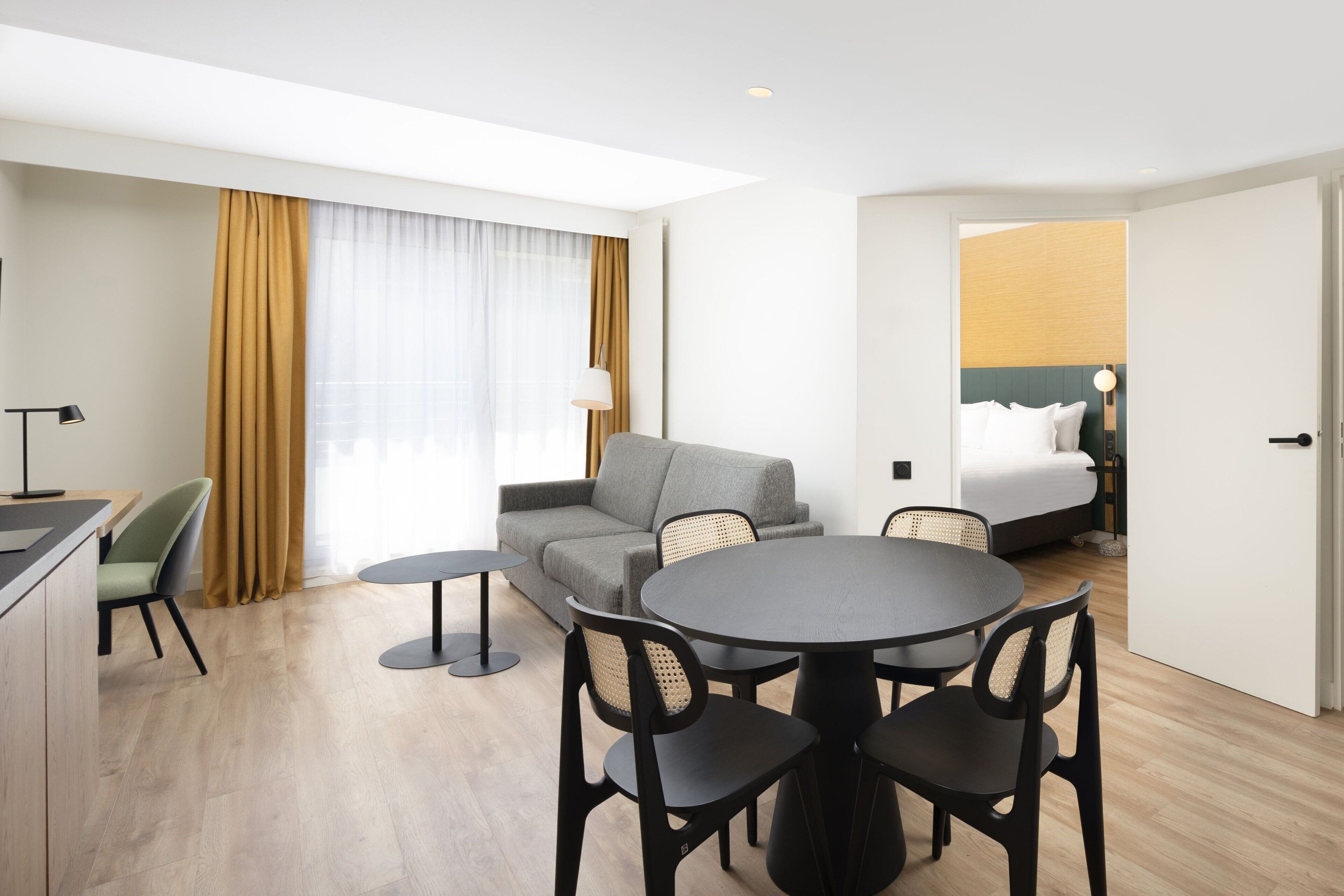 A hotel room with a dining area, a sofa, a bed, and a view of the city.