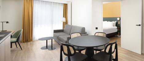 A hotel room with a dining area, a sofa, a bed, and a view of the city.